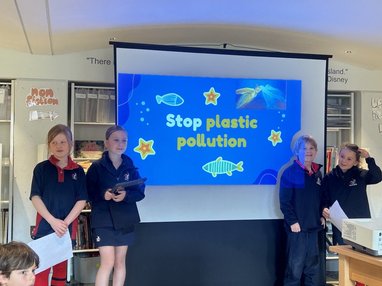4 school children standing in front of a classroom. There is a presentation named "Stop Ocean Pollution" on the whiteboard