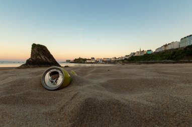 A close up of an aluminium can buried on a sandy beach