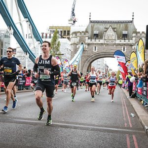 Jim Bourne wears a dark blue marine conservation society running vest. He is photographed running the London Marathon. Tower bridge can be seen behind him along with lots of other runners