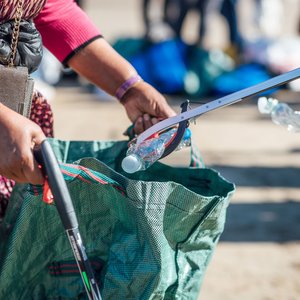 A close up of volunteers filling a bag with plastic bottles at a Scarborough beach clean.