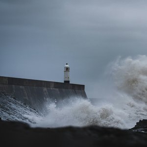 Large white waves hitting a wall at Porthcawl, Wales, with a dark grey sky above the coastline