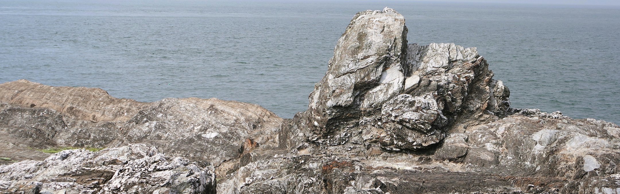 A large, jagged rock formation on the rugged coastline of Ilfracombe Beach, with the sea extending to the horizon under a pale sky.