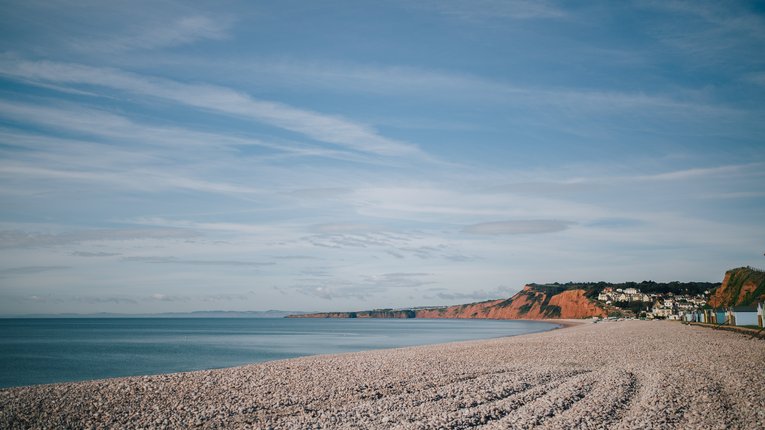 A coastal shot of Budleigh Salterton pebble beach. In the background, the distinctive red cliffs can be seen.