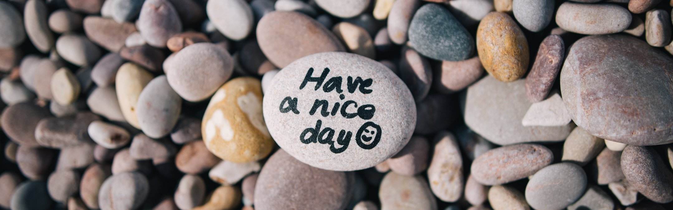 A top down views of a pebble beach up close. On the pebble in the middle, a message written on it reads "Have a nice day" followed by a smiley face.