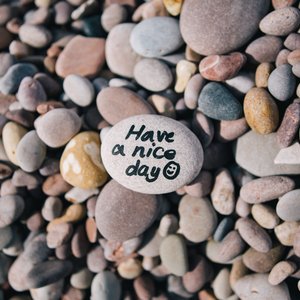 A top down views of a pebble beach up close. On the pebble in the middle, a message written on it reads "Have a nice day" followed by a smiley face.