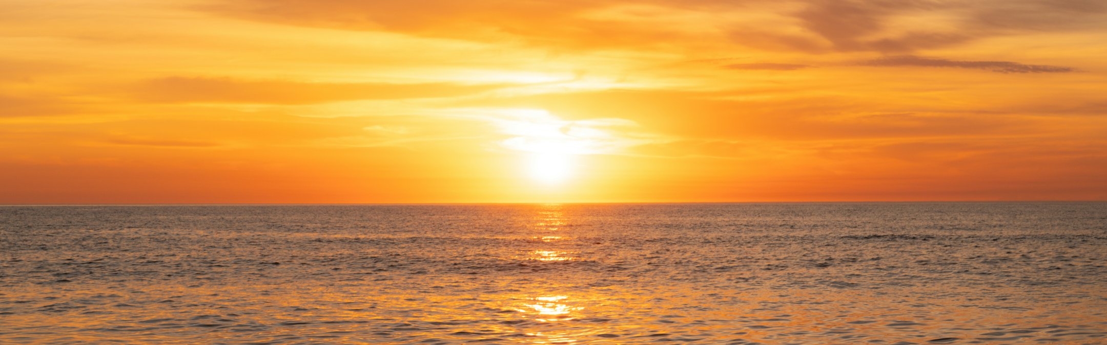 A shot of the open water during a sunset. The entire ocean surface is glowing orange
