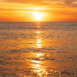 A shot of the open water during a sunset. The entire ocean surface is glowing orange