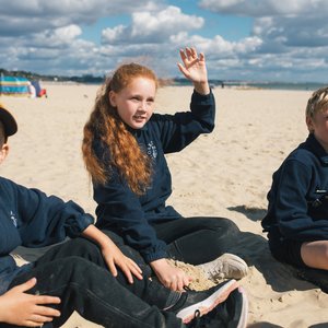 A young girl sitting on a beach with her hand up