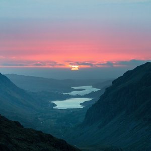 The sun is pictured rising from the top of Mount Snowdon. The sky is pink and orange as the sun is slowly rising, its beams reflected on the water in the valley