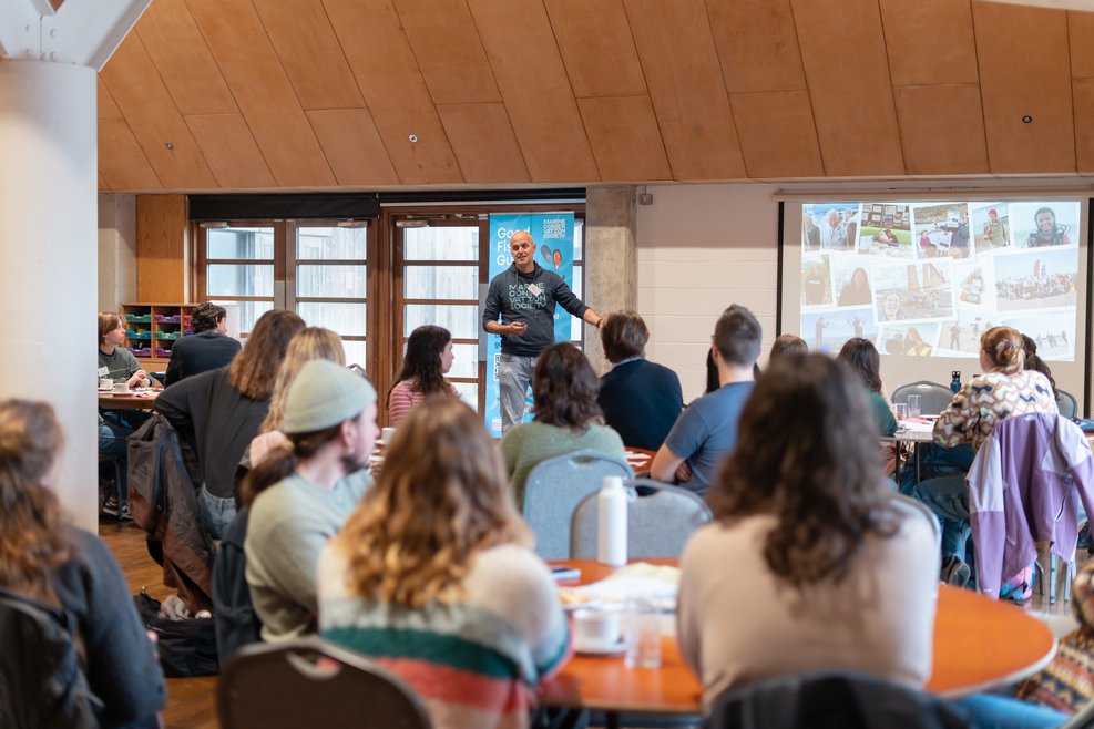 A member of the Ocean Learning team speaking to a group of residents. On the whiteboard is a presentation on volunteering.