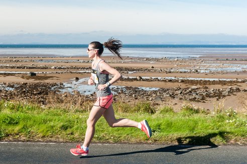 A runner on a paved path next to a rocky shoreline and the sea.